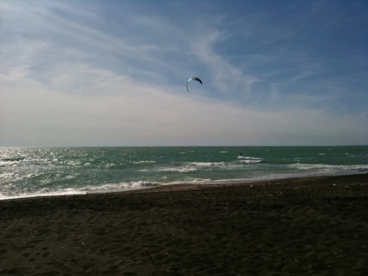 the beach in front of a wave crashing and people flying a kite