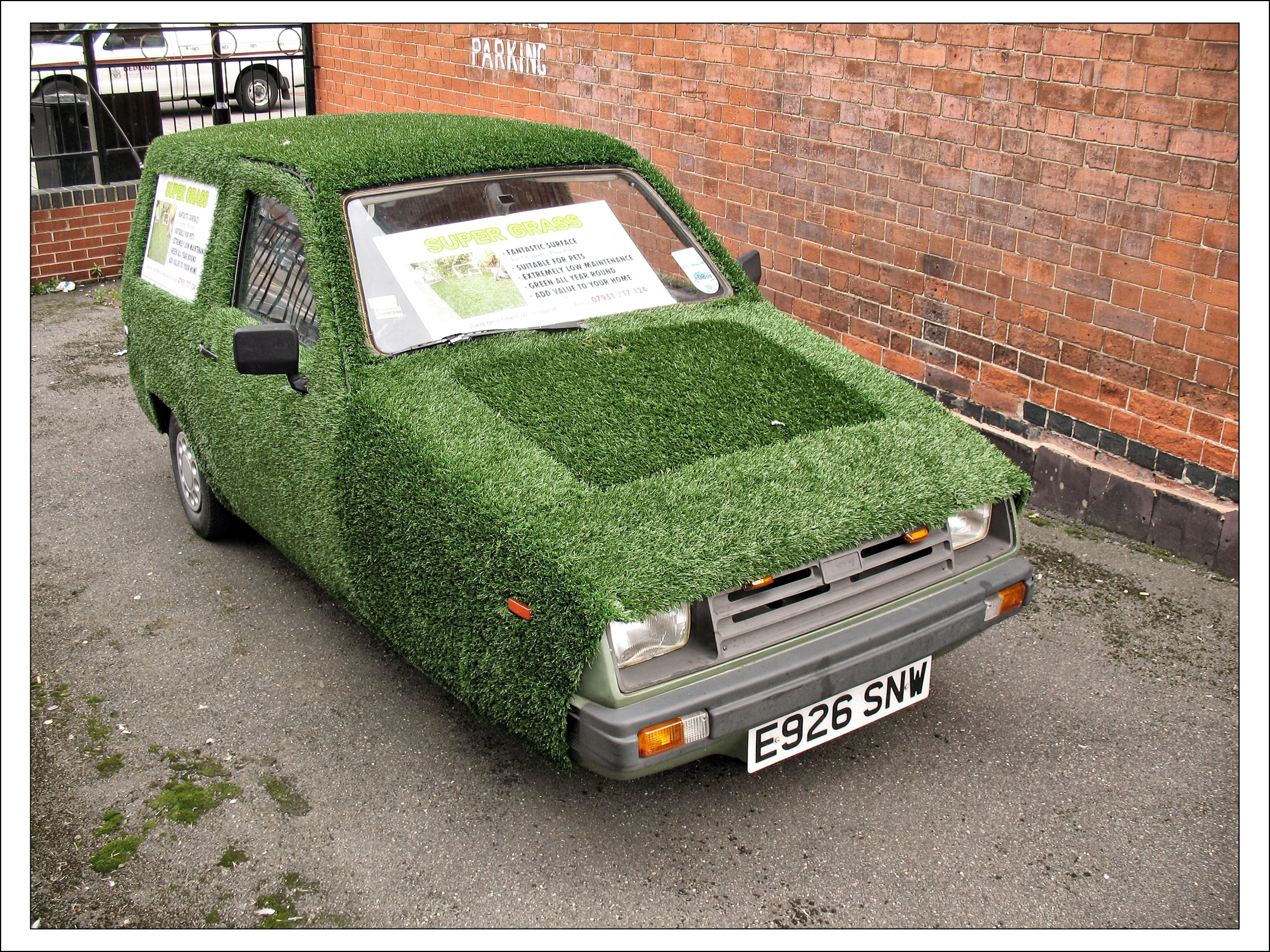 a car covered in grass in front of a brick building