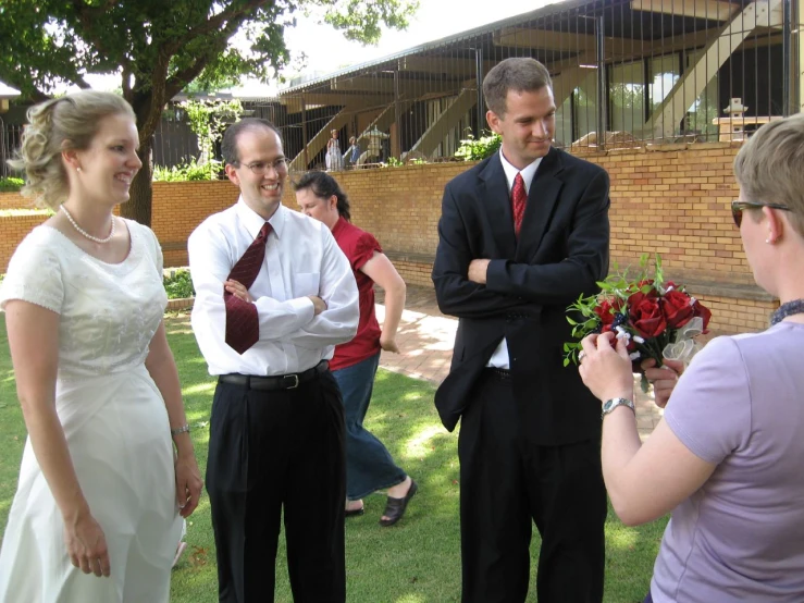 two men and a woman in formal wear standing in the grass with bouquet