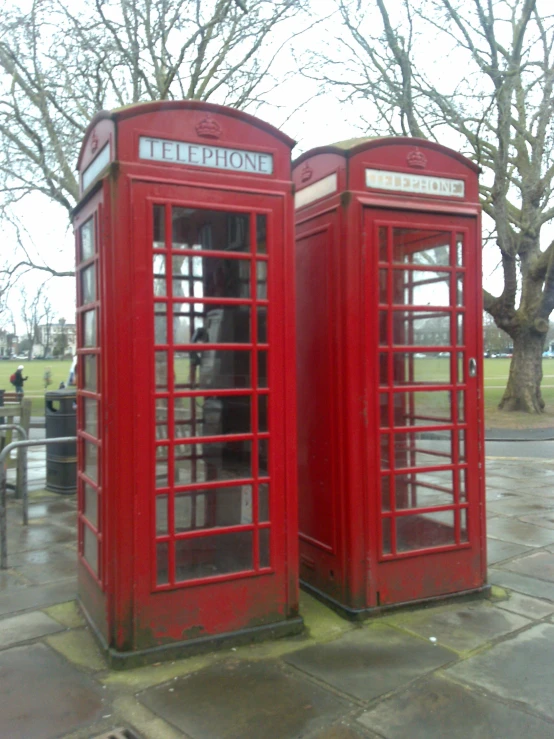 two red telephone booth on sidewalk near trees