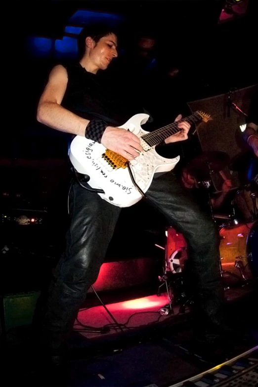 a man standing up while holding a white guitar