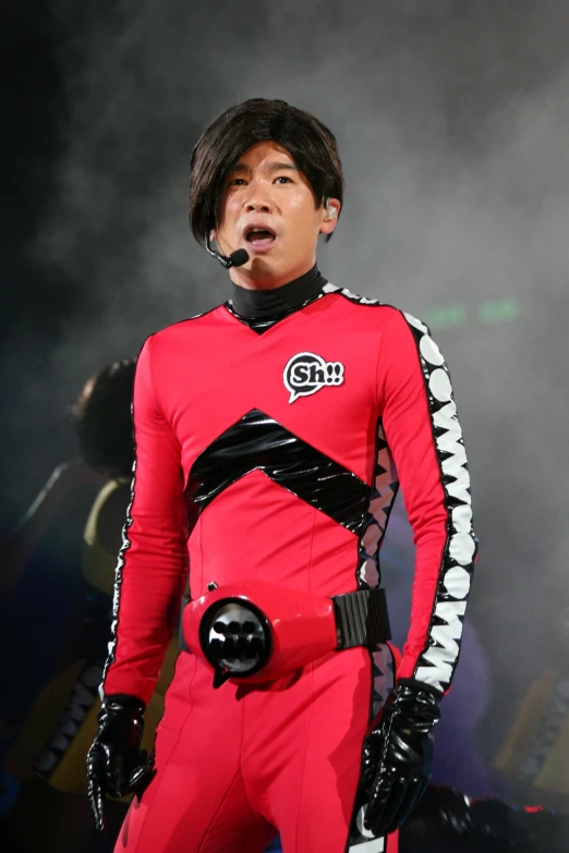 an asian man wearing a bright red outfit standing in front of smoke