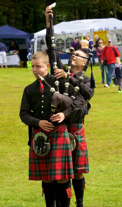 two men in tartans and one is playing the bagpipe