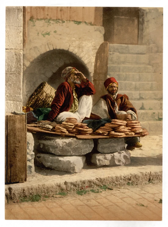 a couple of men sit outside next to some stacked bags