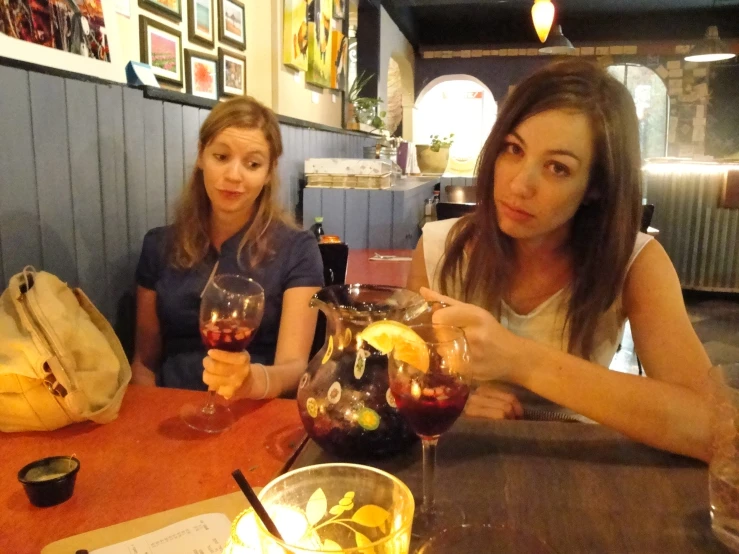 two women seated at a table with glasses of wine and fruit