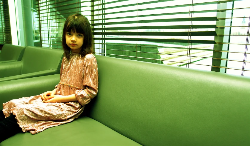 a small girl in a brown dress sitting on a green sofa