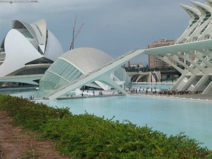 a group of people walk next to water outside of an unusual looking building