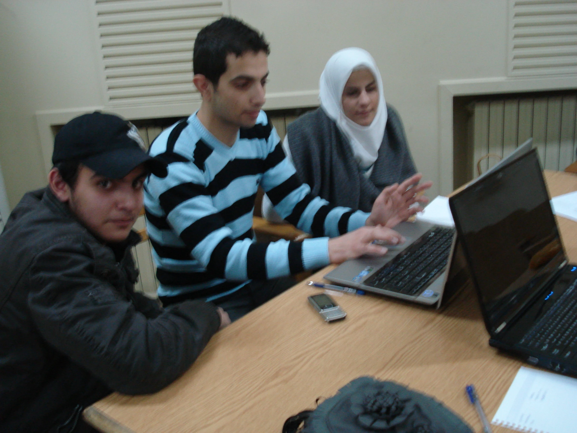 several people sitting around a table, working on laptops