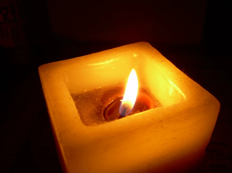 lit wax candle in a square container on a table