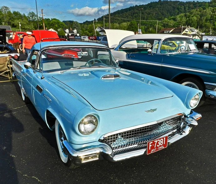 an old - fashioned blue car with the hood up sits parked next to another older one