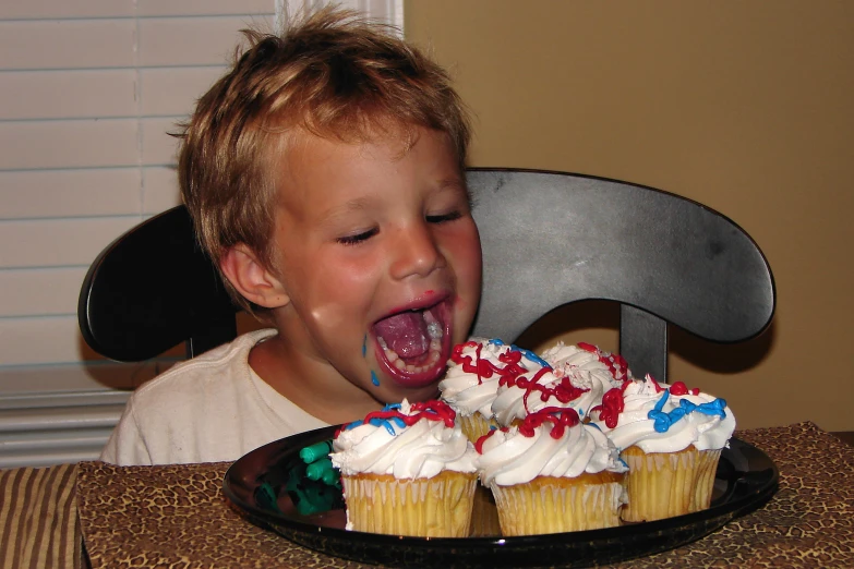 the child is biting into the cupcakes with their mouth wide open