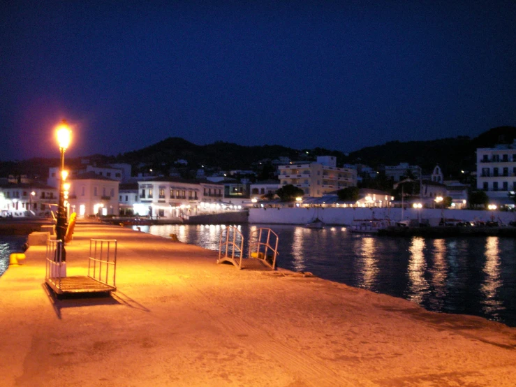 an empty shore line at night, with the water and city lights