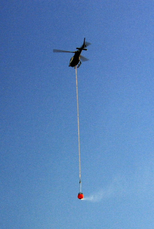 a helicopter flying overhead with a parachute hooked to it