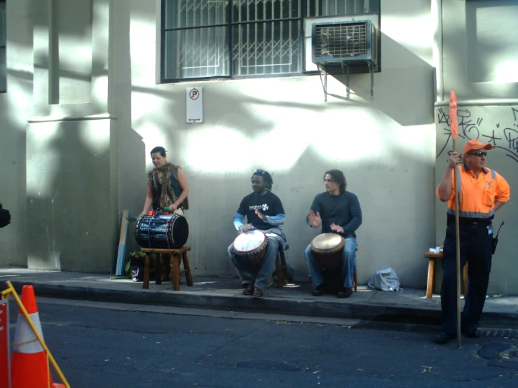 a group of people sitting on a street side playing musical instruments