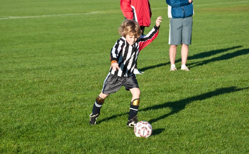 three boys on a field playing soccer with one of them wearing yellow boots