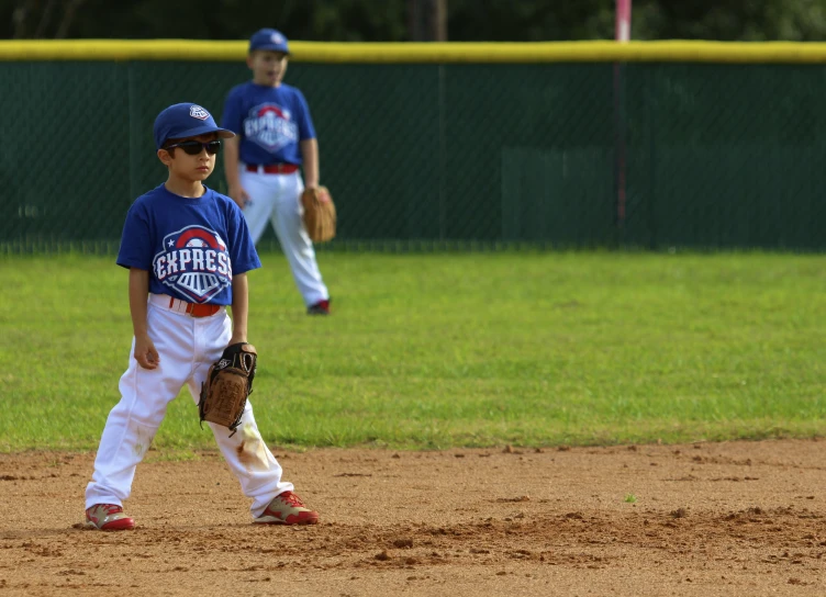 two boys in blue and white baseball uniforms walking along a field