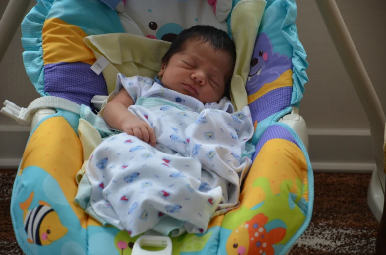 a newborn baby sleeps in a bouncer and is looking off into the distance