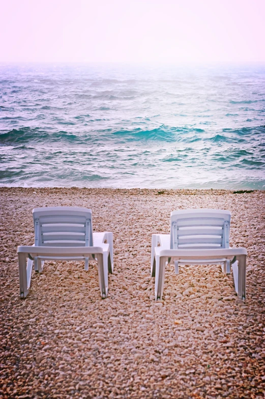 two plastic chairs sit on the beach near the ocean