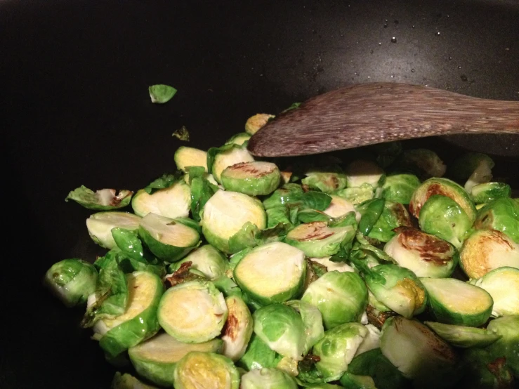 a wooden spoon being used over a pot of brussels sprouts
