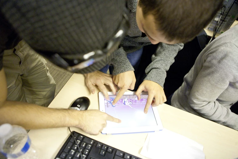 several people sitting at a table looking at an electronic device