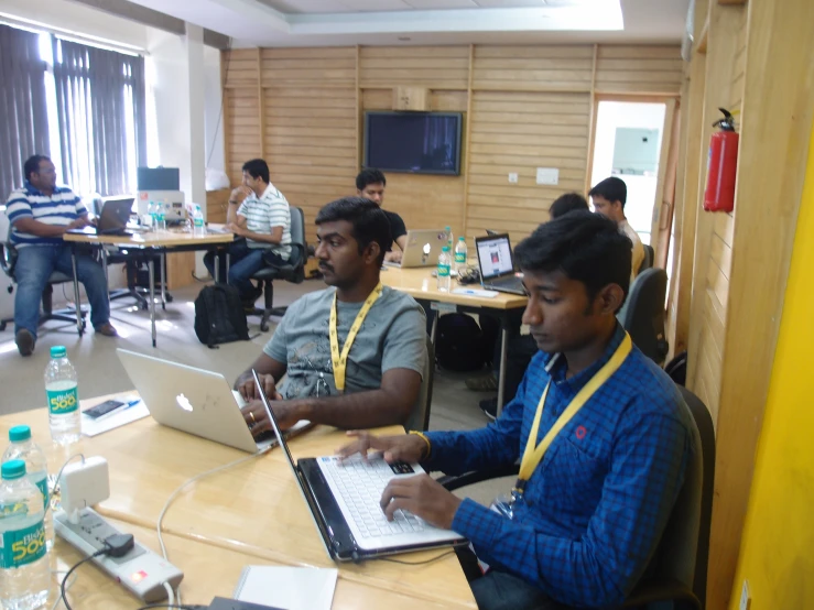 four men sitting at a long table working on computers