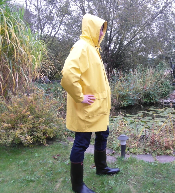 a man standing in front of a pond wearing a yellow raincoat and black boots