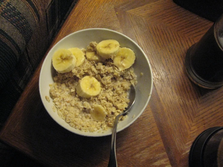 bowl with oatmeal and bananas on top sitting next to cup with spoon