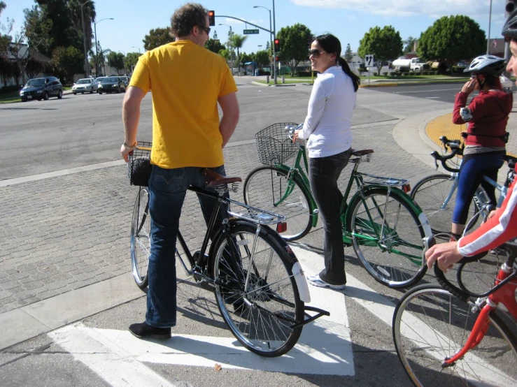 two women and one man on bikes waiting at the crosswalk