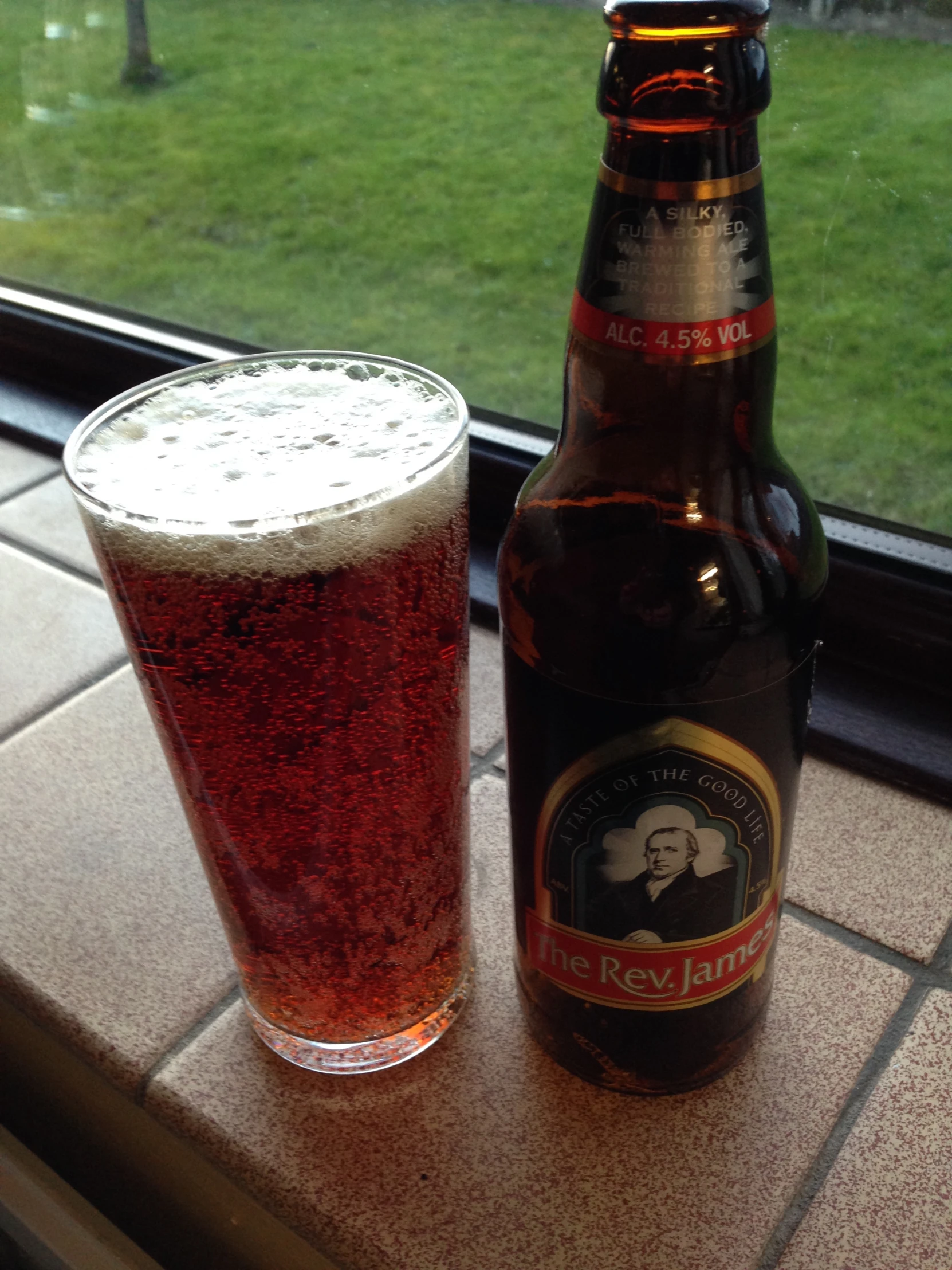 beer glass and bottle sit in front of a window