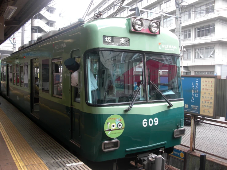 a green train pulling into a station with a person waiting on it
