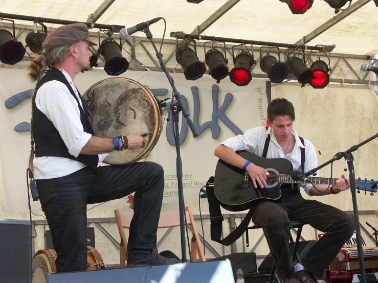 two men sit on stage playing guitar and singing