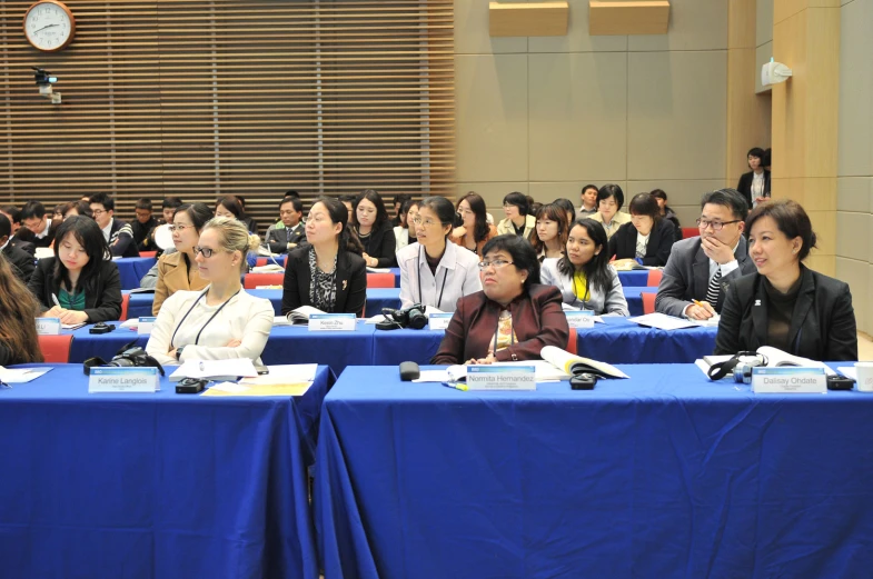 several people sitting at blue tables talking in an auditorium