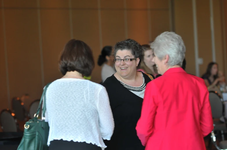 two ladies are smiling and having conversation in front of another woman