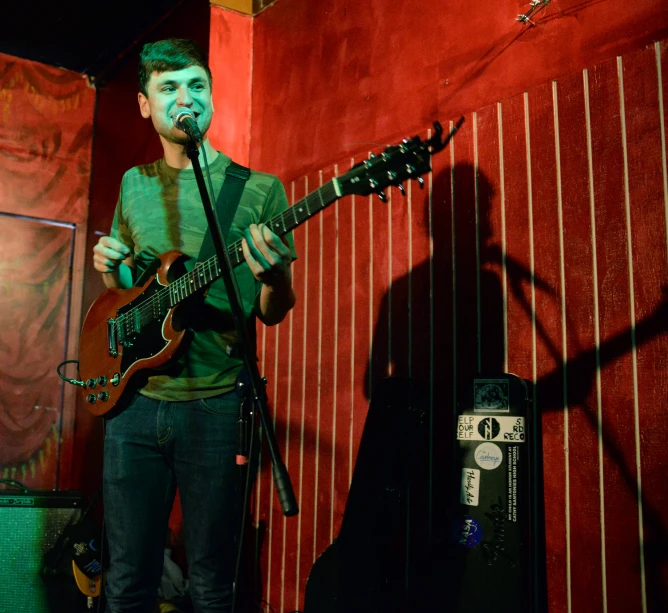 a young man standing next to a microphone holding a guitar