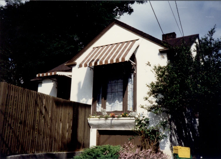 a house with a white wall and wooden trimming on the windows and a brown striped awning above it