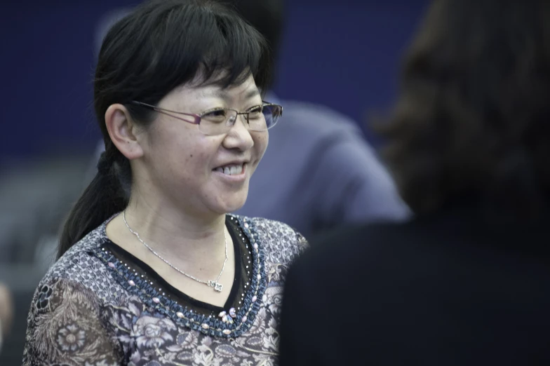 a woman with glasses smiles and talks to other people