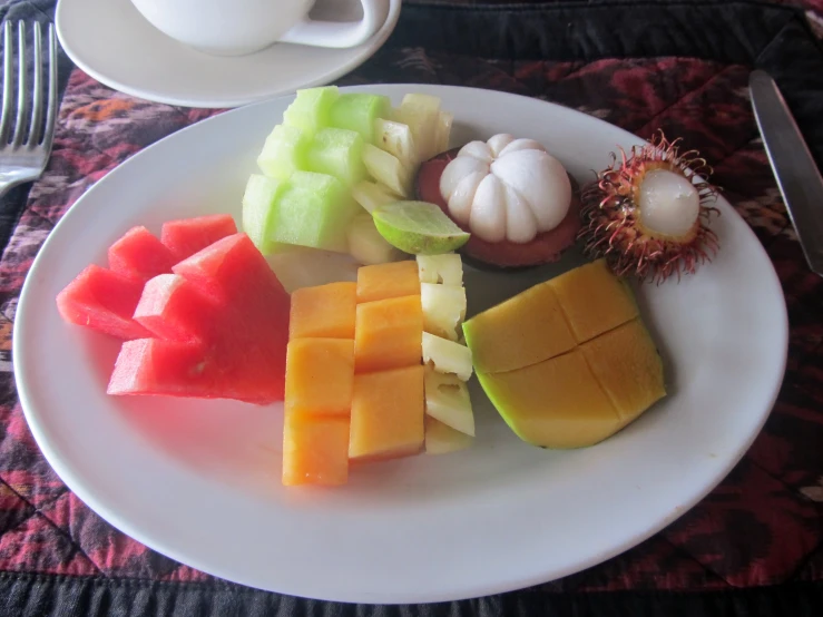 various fruit is cut on a plate along with a mug