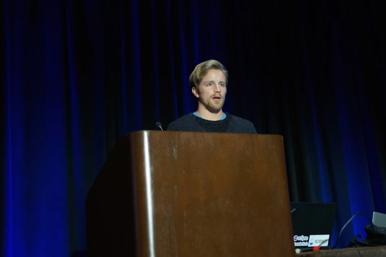 a man talking behind a wooden podium on stage