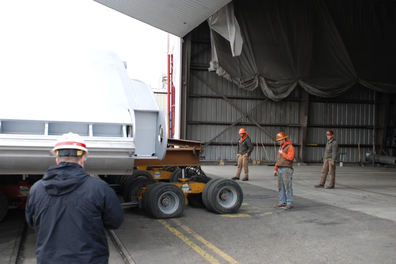 three men stand next to a trailer with large tire wheels