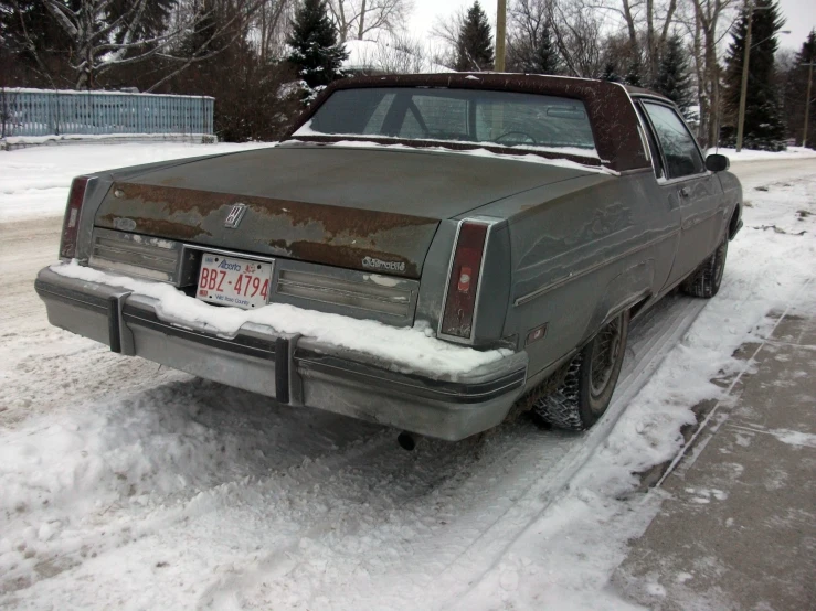 a rusty vintage car parked on a snow covered parking lot