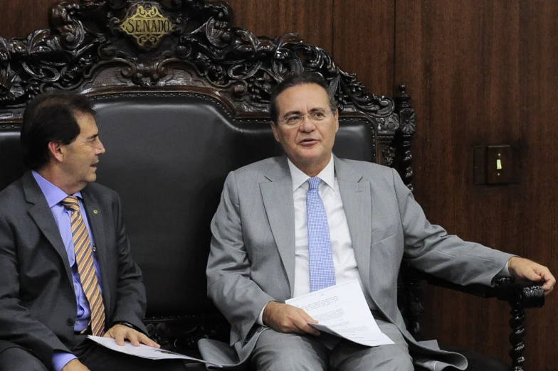 two men sitting in a chair, with papers on the table