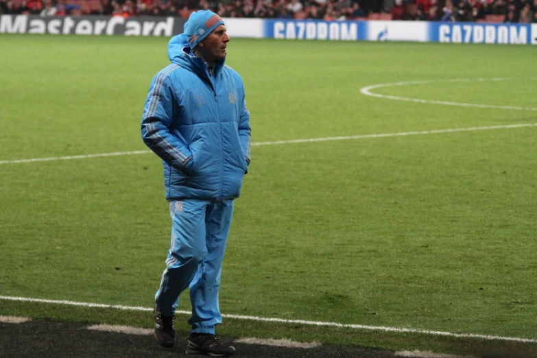 a man in a blue snow suit standing in front of a soccer field