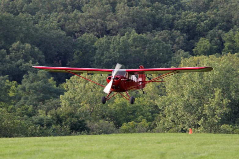 a small red plane flying low over a lush green field