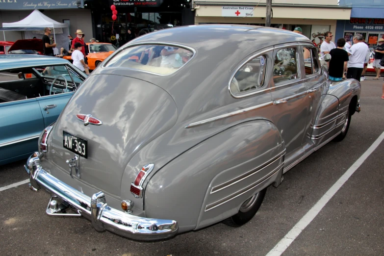 an old gray car parked on a road near other antique cars