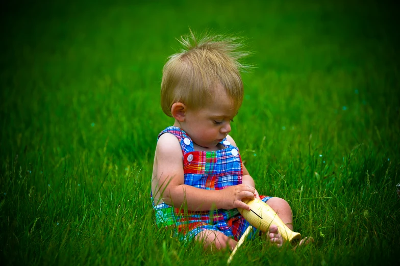 a little boy sitting in the grass eating a banana