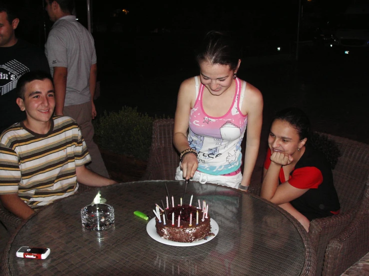 people gathered around a table with a chocolate cake on it