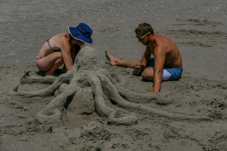 two men work on an octo sculpture while sitting in the sand
