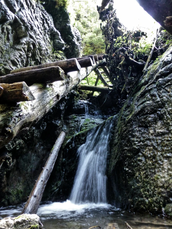 the water flowing over a small wooden bridge in a rocky stream