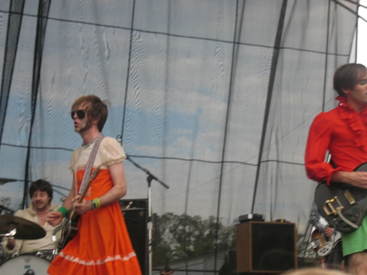 the man is dressed in orange, the woman is on stage with a guitar