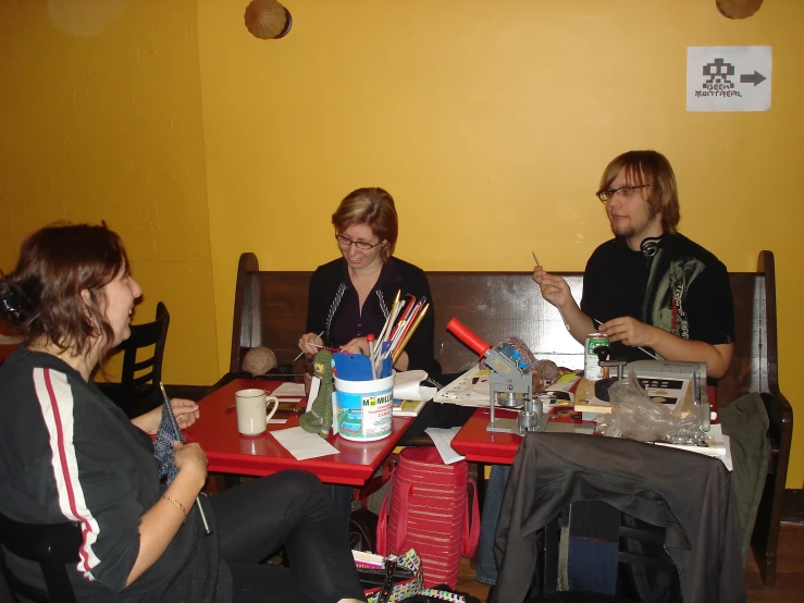 three ladies sit at a table with cups, pencils and papers